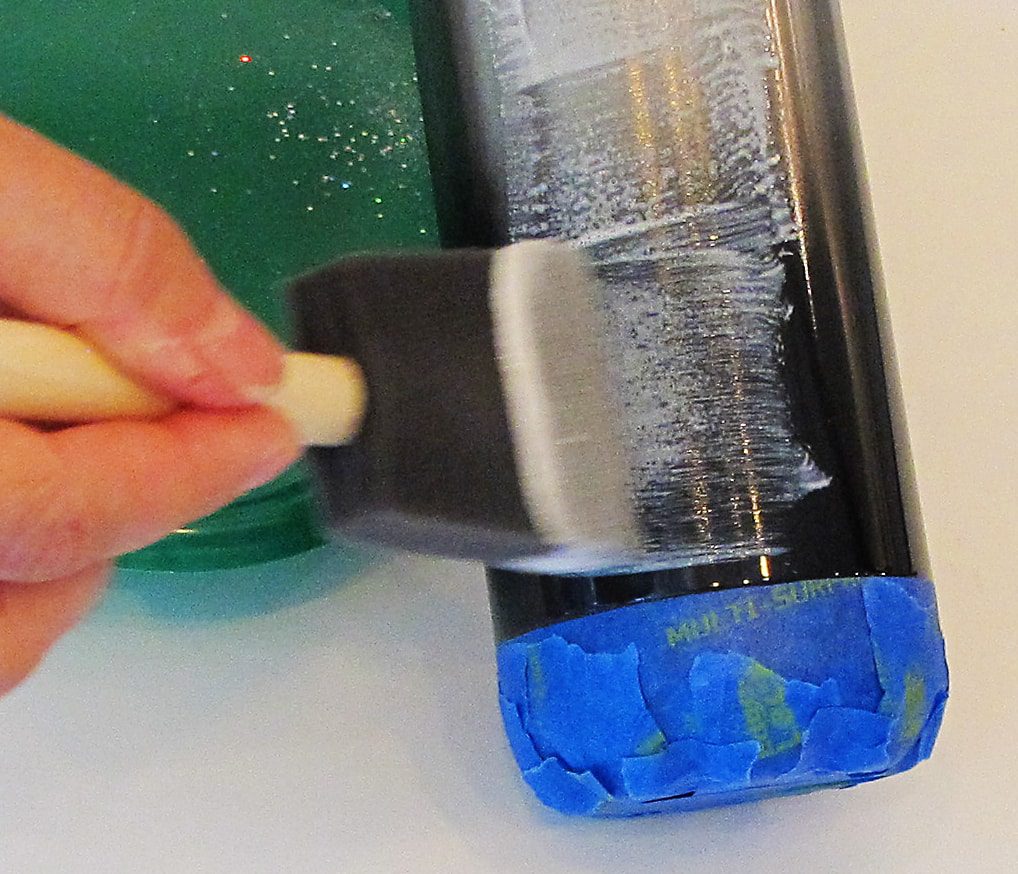 applying glue to a stainless steel tumbler with a foam brush