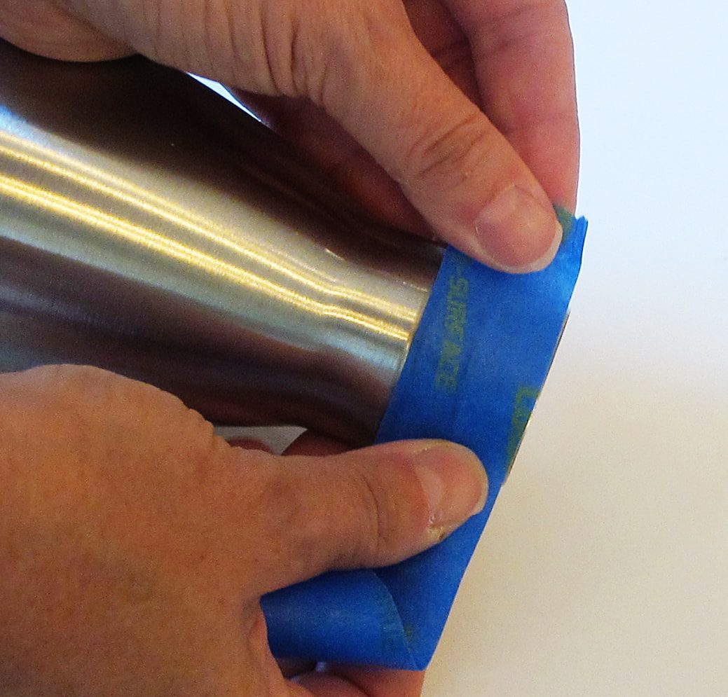 applying painters tape to both ends of a stainless steel tumbler