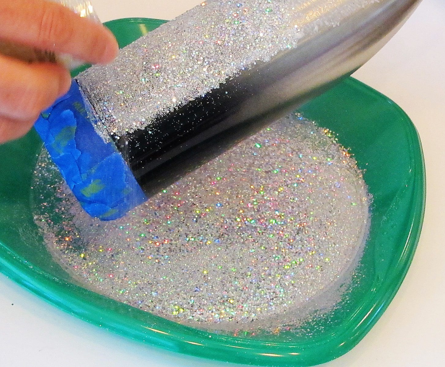 applying glitter to the glued area on a stainless steel tumbler