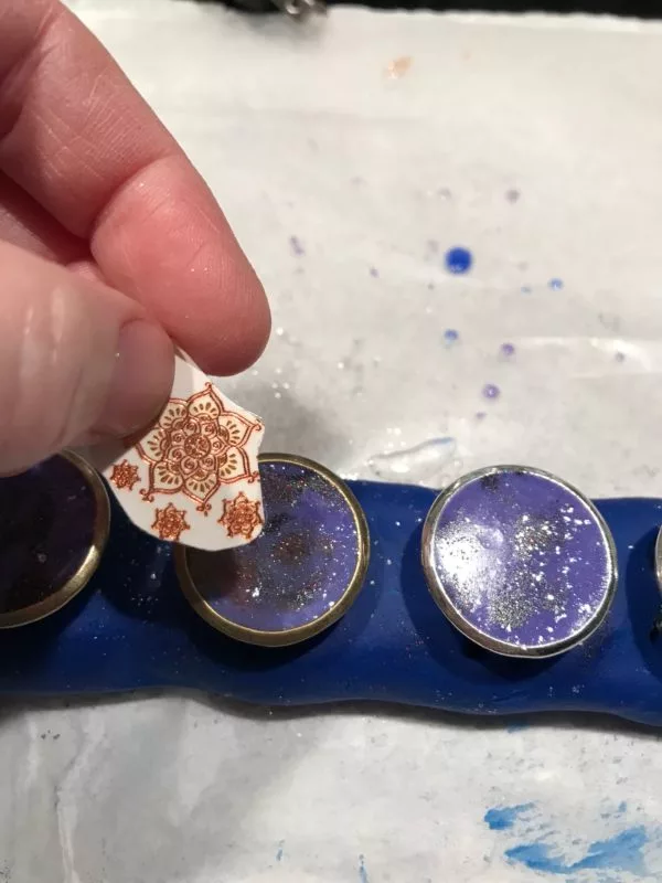 Applying mandala temporary tattoo to rings with deep purple resin background