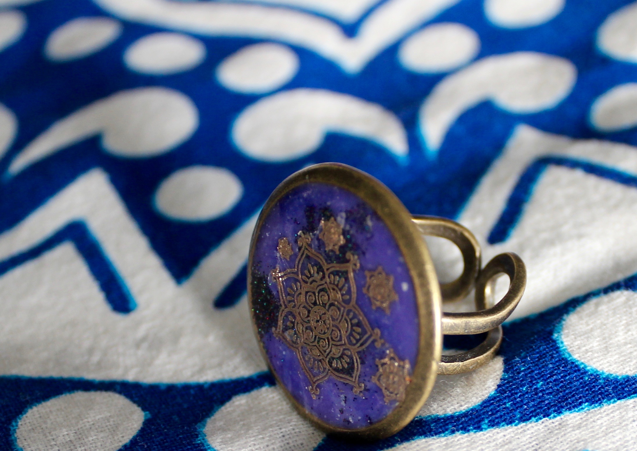 Close-up of ring with gold mandala designs on deep purple resin background