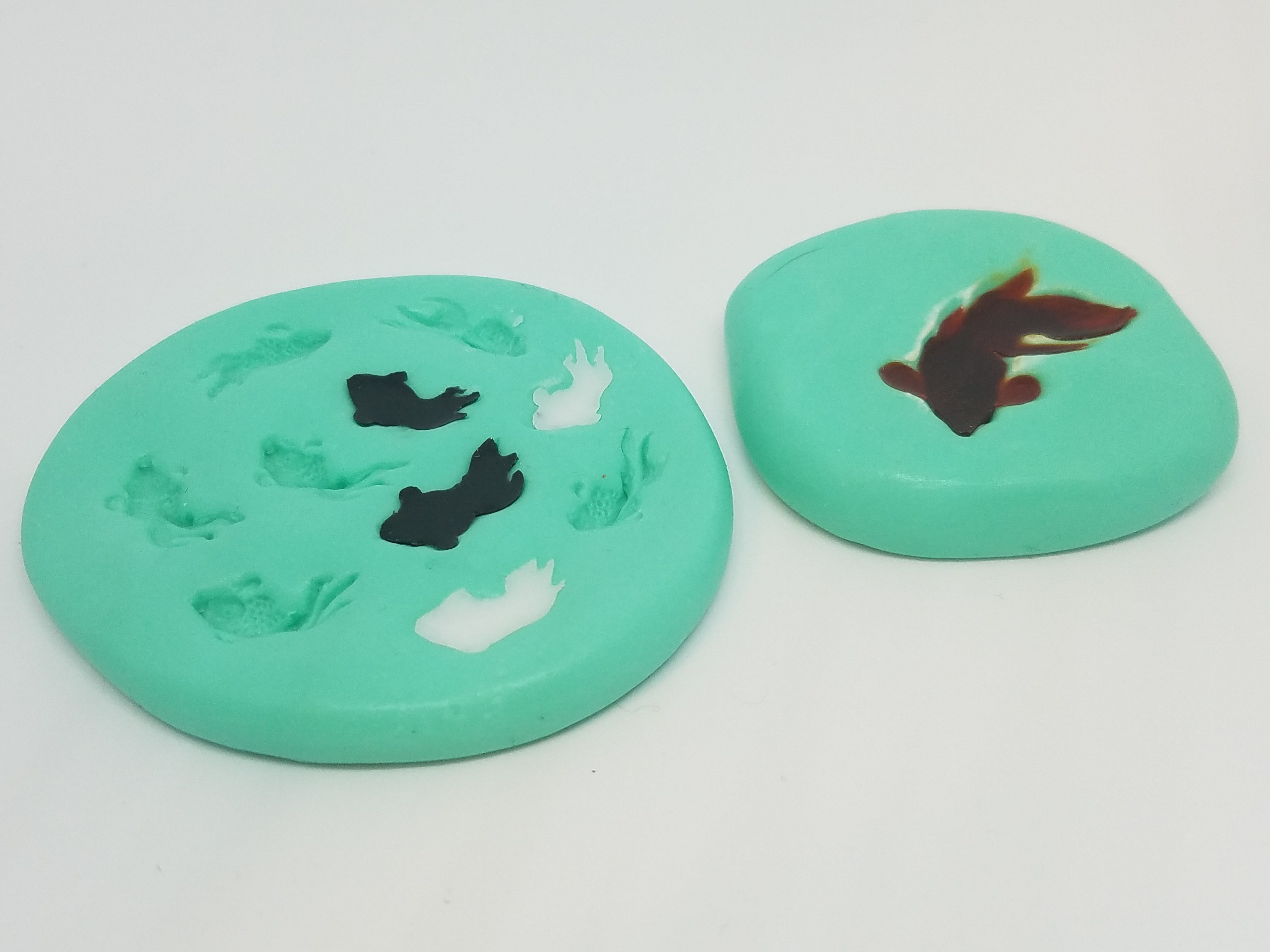 Two green koi molds filled with white, black, and orange resin