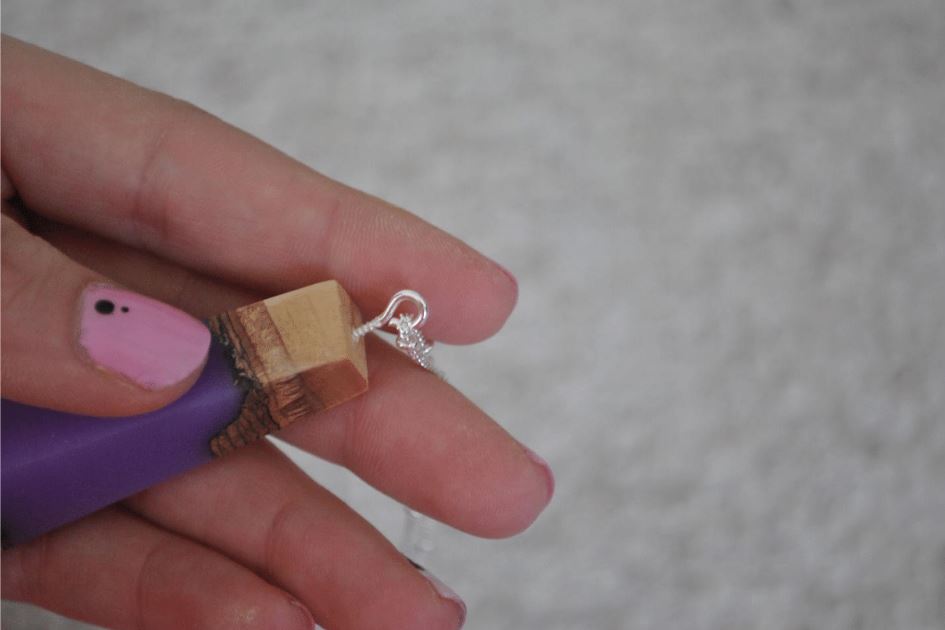 left hand holding wood and lavender resin pendant with eyehook and chain