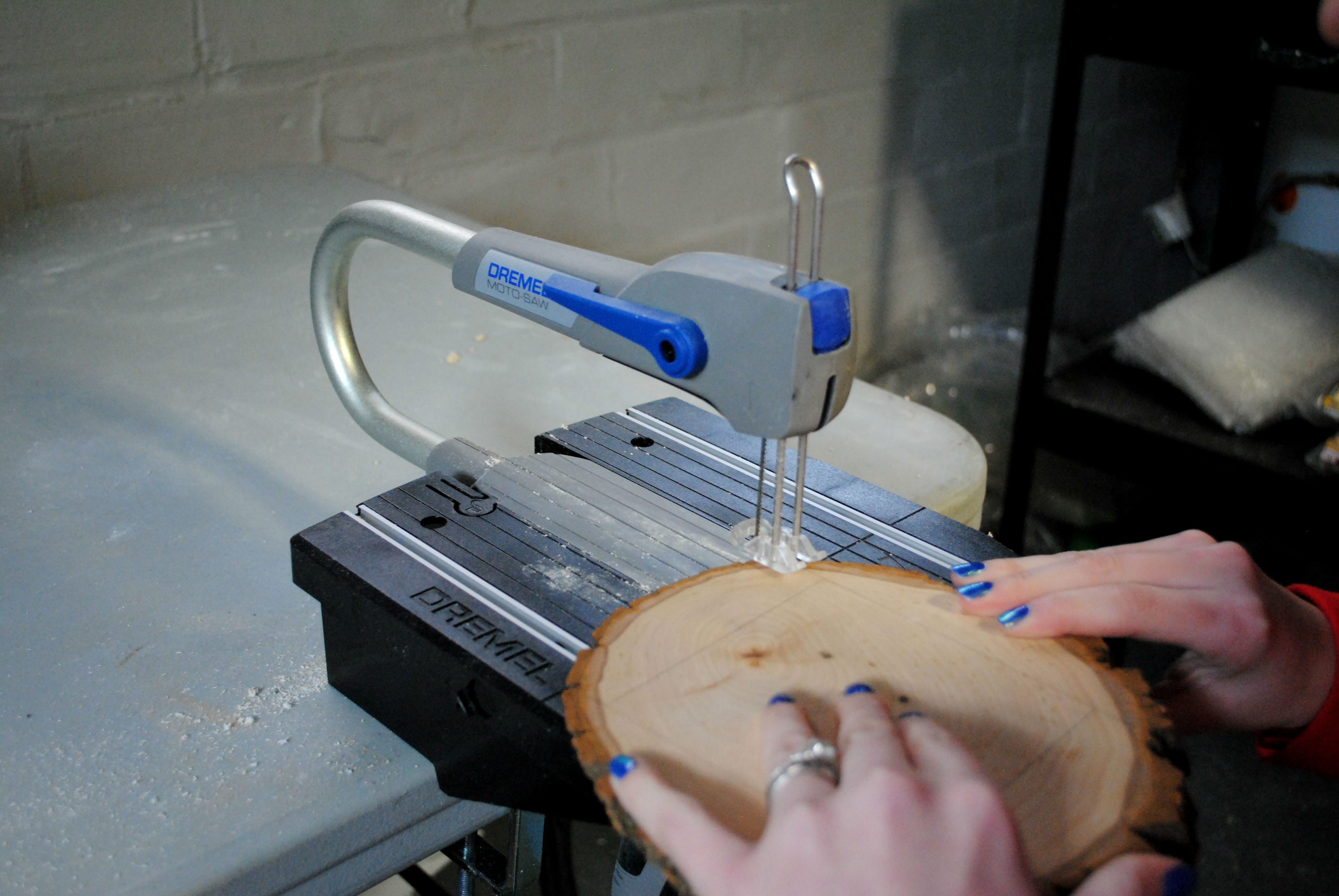 hands holding slice of wood and cutting it with a dremel moto saw