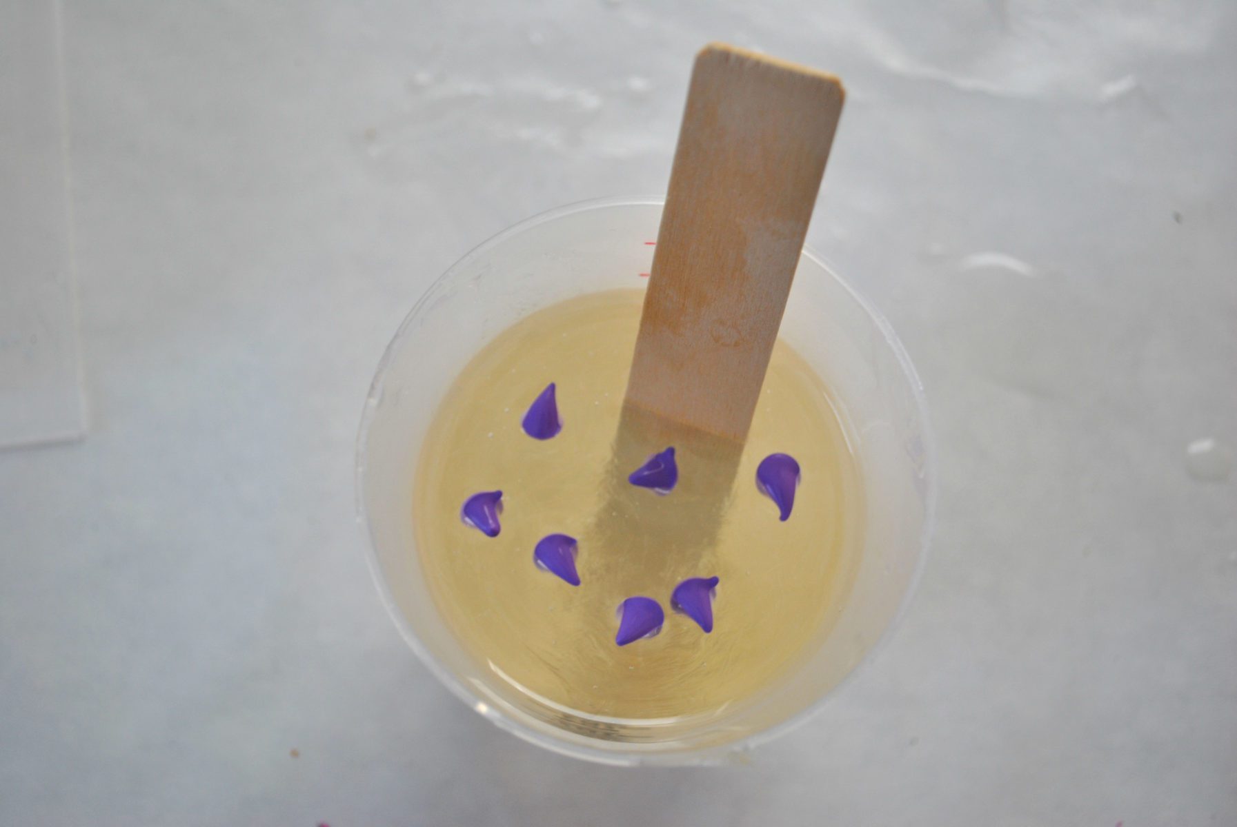resin mixture in a cup with wooden stirrer with droplets of lavender resin dye
