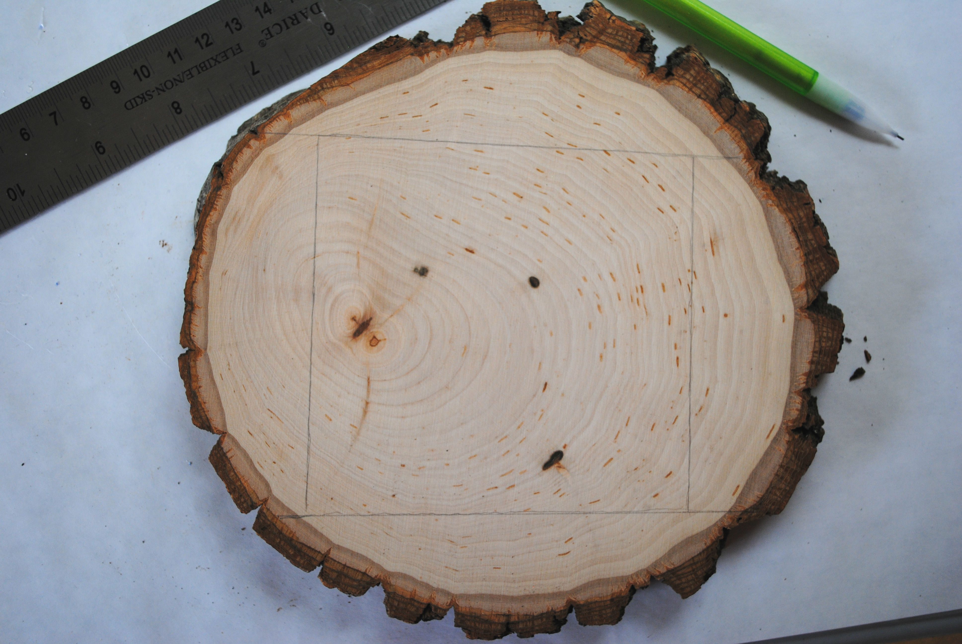 slice of wood with measurements for cutting drawn on and a ruler and a pencil