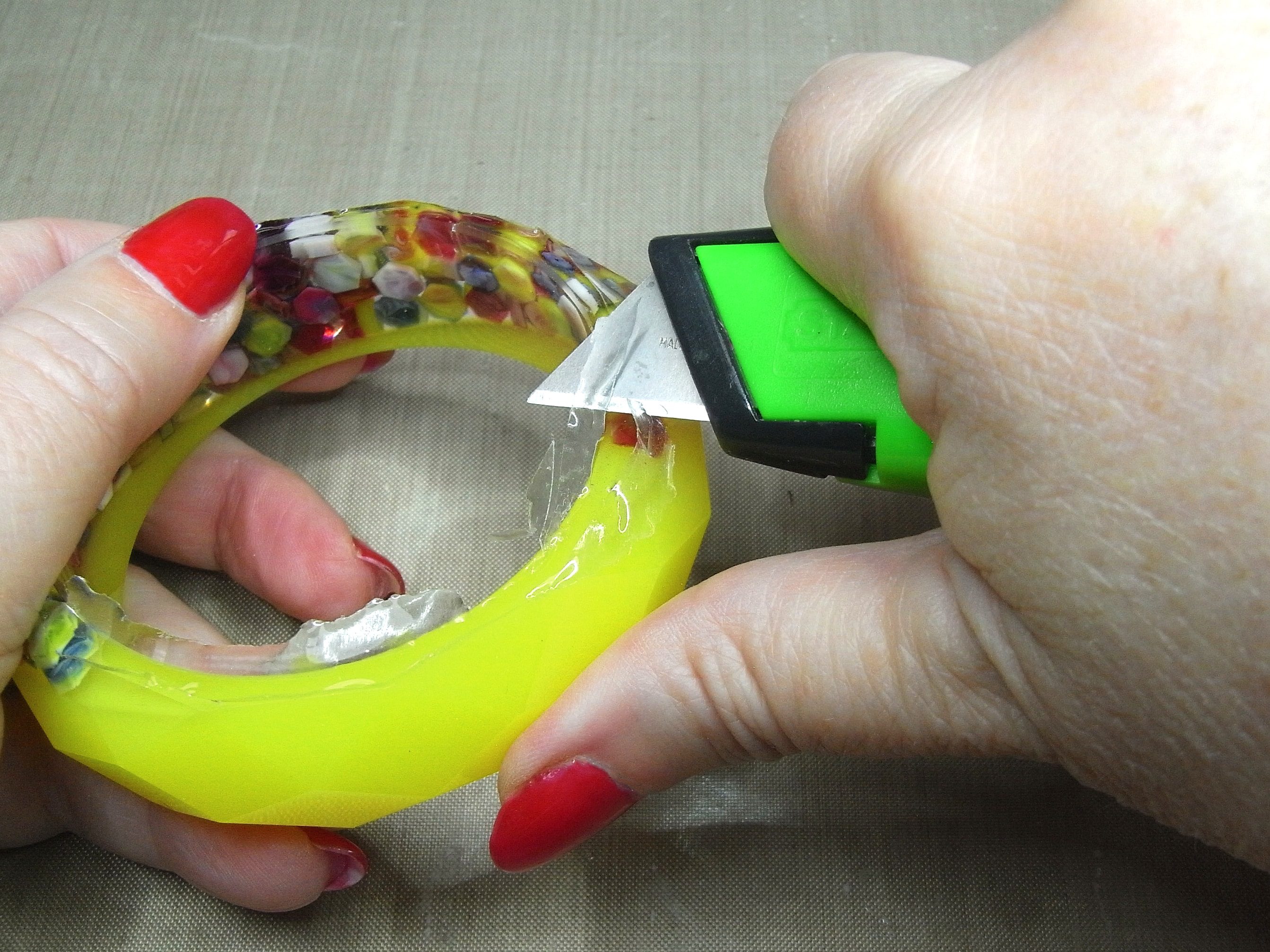 trimming away rough edges of resin bangle with utility knife