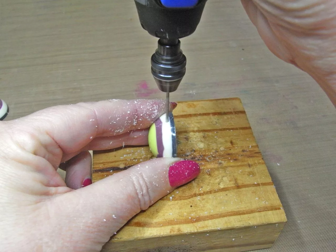  drilling a hole in a resin charm on a wood block