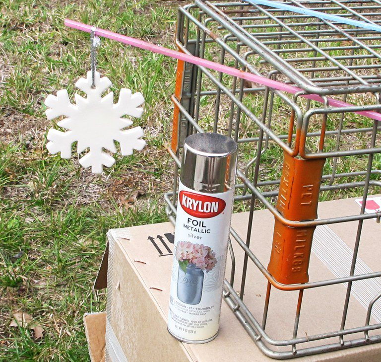Can of spray paint and hanging snowflake ornament with pet cage outside.
