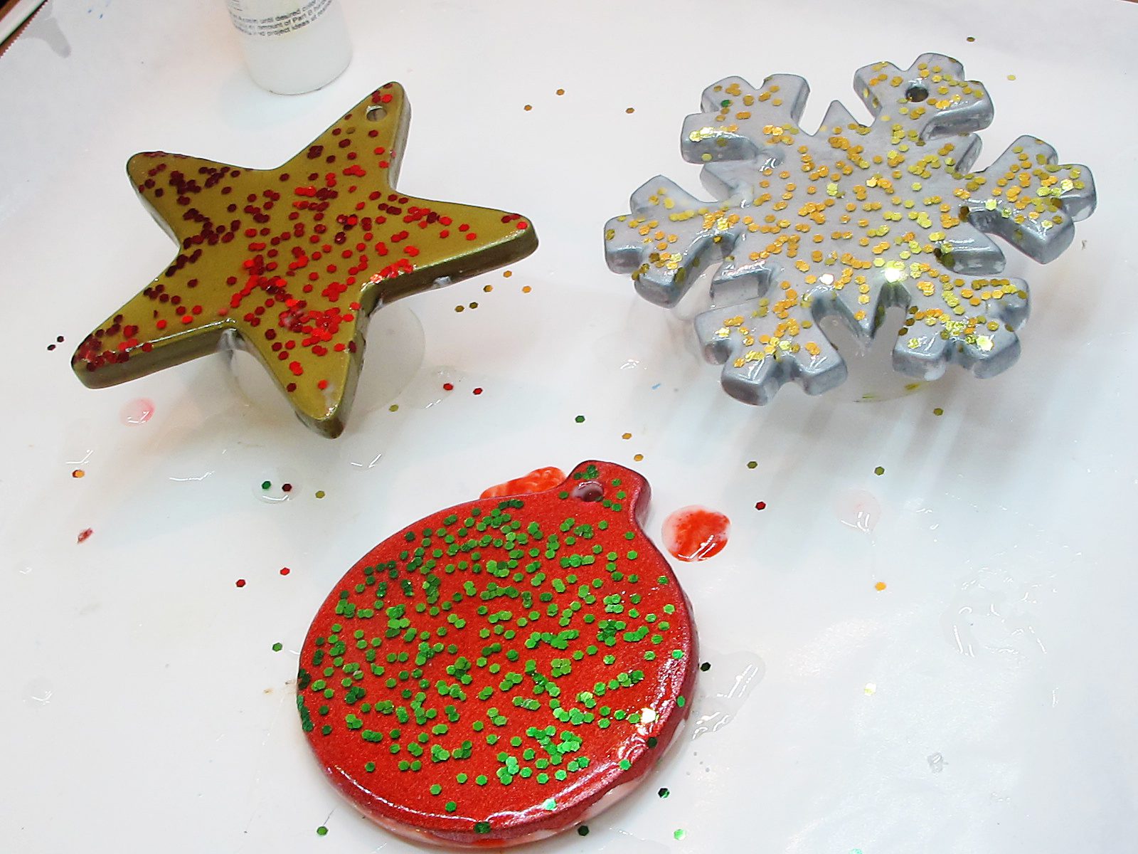 Glittery front side of three resin Christmas ornaments.